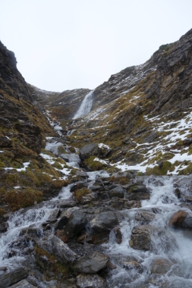 A defrosted ravine with a roaring cascade cutting through it.